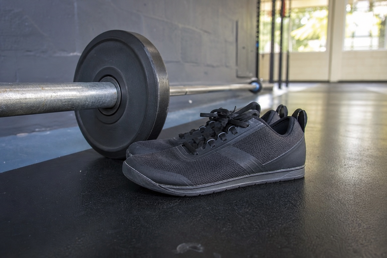 Chaussures de crossfit à semelle plate posées à côté d'une barre de musculation en salle de sport