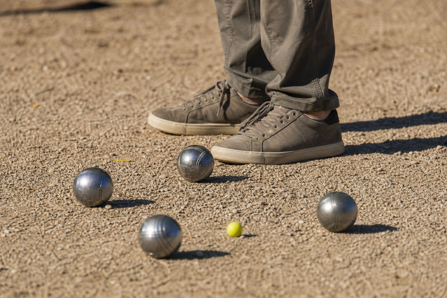 Chaussures basses posées sur un terrain de pétanque en gravier, à côté de boules de pétanque